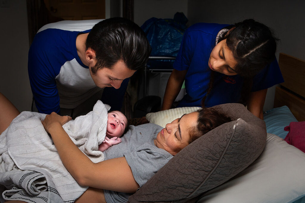 color home birth photo of a newborn looking at his father by Birth and Beauty.