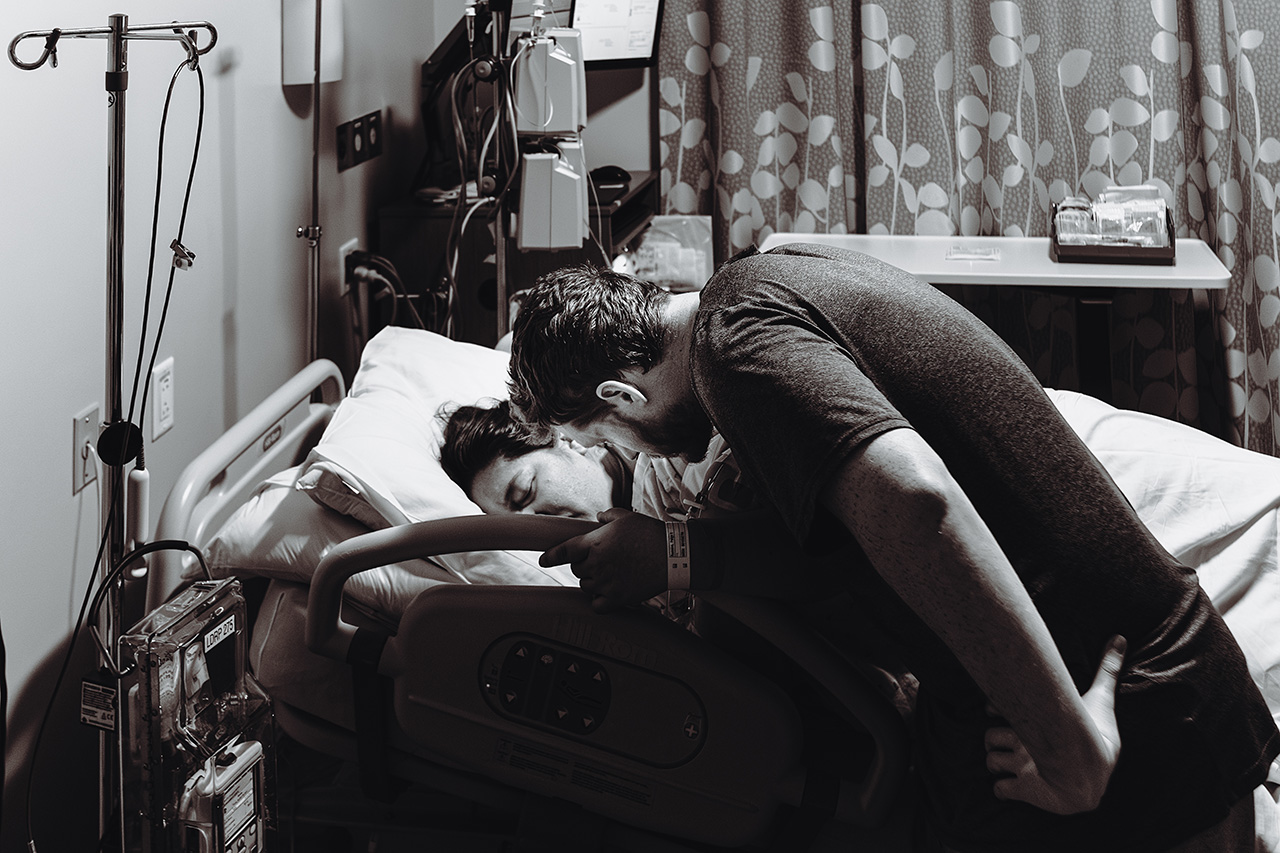 Black and white image of a husband comforting his wide during active labor. Photo by birth photographer, Leona Darnell.