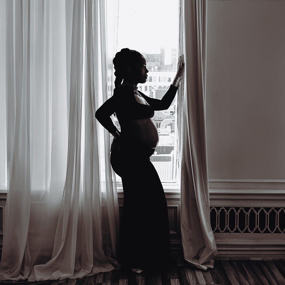 black and white pregnancy portrait of a black woman against a window by Birth and Beauty.