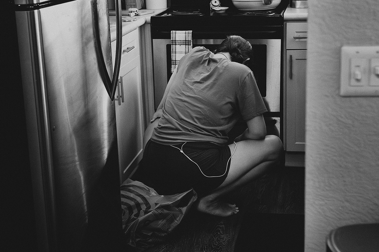 A black and white image by Birth and Beauty showing a woman in labor squatting in the kitchen of her home. 